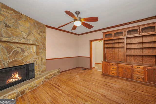 unfurnished living room with ceiling fan, a fireplace, ornamental molding, and light wood-type flooring