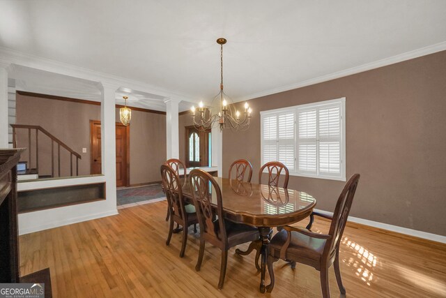 dining space featuring light hardwood / wood-style floors, ornate columns, ornamental molding, and an inviting chandelier