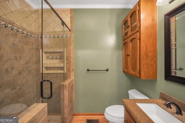 bathroom featuring ornamental molding, vanity, a shower with door, hardwood / wood-style flooring, and toilet