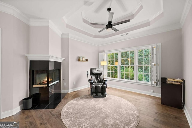 bedroom featuring ornamental molding, a raised ceiling, ceiling fan, hardwood / wood-style flooring, and a tiled fireplace