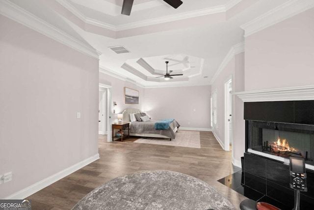 bedroom with a tile fireplace, ceiling fan, a tray ceiling, hardwood / wood-style flooring, and ornamental molding