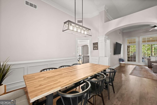 dining room featuring ornate columns, crown molding, ceiling fan, and dark wood-type flooring