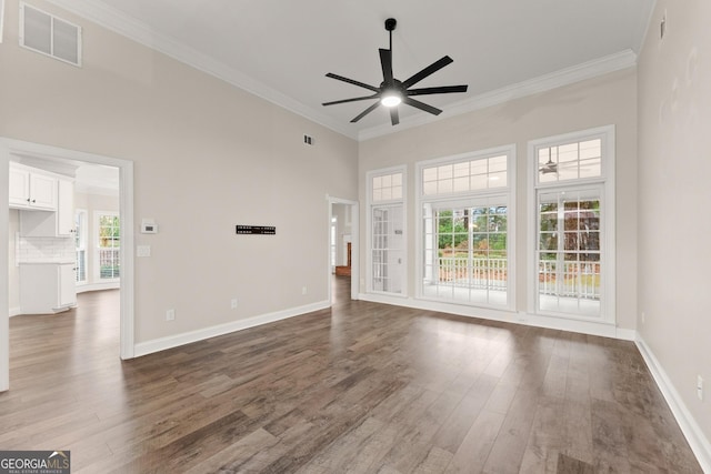 unfurnished living room with dark hardwood / wood-style floors, ceiling fan, ornamental molding, and a towering ceiling