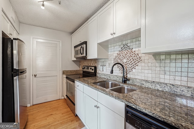 kitchen with white cabinetry, dark stone counters, light hardwood / wood-style flooring, sink, and stainless steel appliances