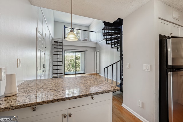 kitchen with light hardwood / wood-style flooring, hanging light fixtures, dark stone countertops, white cabinets, and stainless steel refrigerator