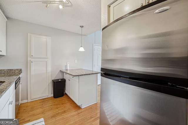 kitchen with pendant lighting, white cabinets, stainless steel appliances, and light wood-type flooring