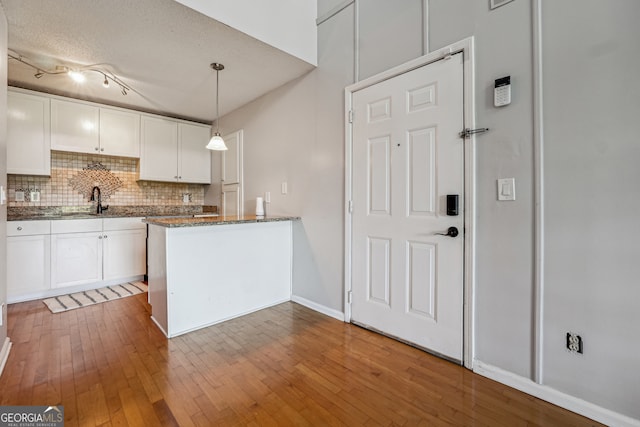 kitchen featuring a textured ceiling, white cabinetry, pendant lighting, hardwood / wood-style flooring, and decorative backsplash