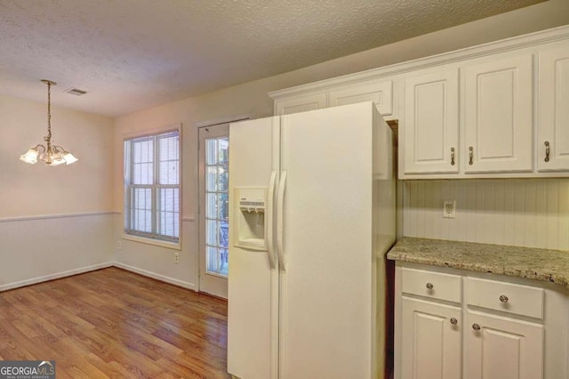 kitchen with white cabinetry, a textured ceiling, light wood-type flooring, decorative light fixtures, and white refrigerator with ice dispenser