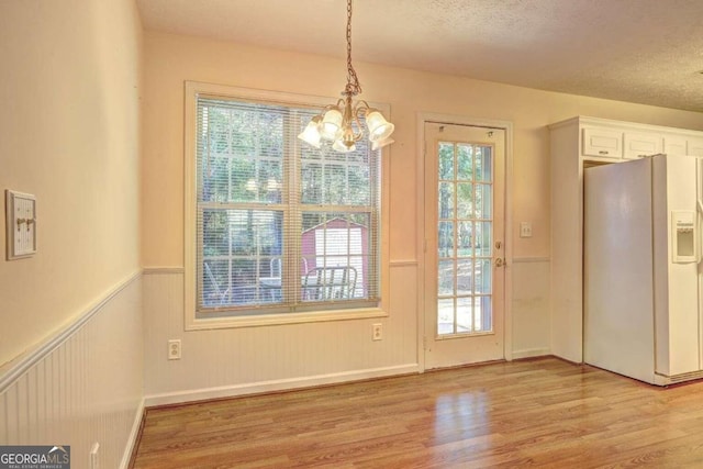 unfurnished dining area featuring a notable chandelier, a textured ceiling, and light hardwood / wood-style floors