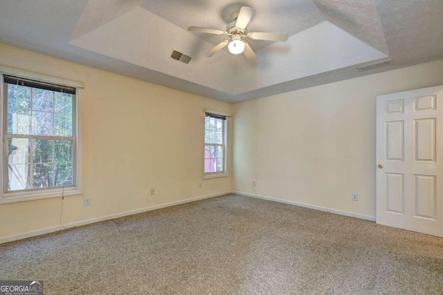 spare room with ceiling fan, a raised ceiling, carpet floors, and plenty of natural light