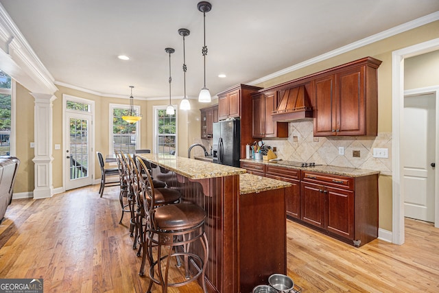 kitchen with ornate columns, light hardwood / wood-style flooring, stainless steel fridge with ice dispenser, pendant lighting, and premium range hood