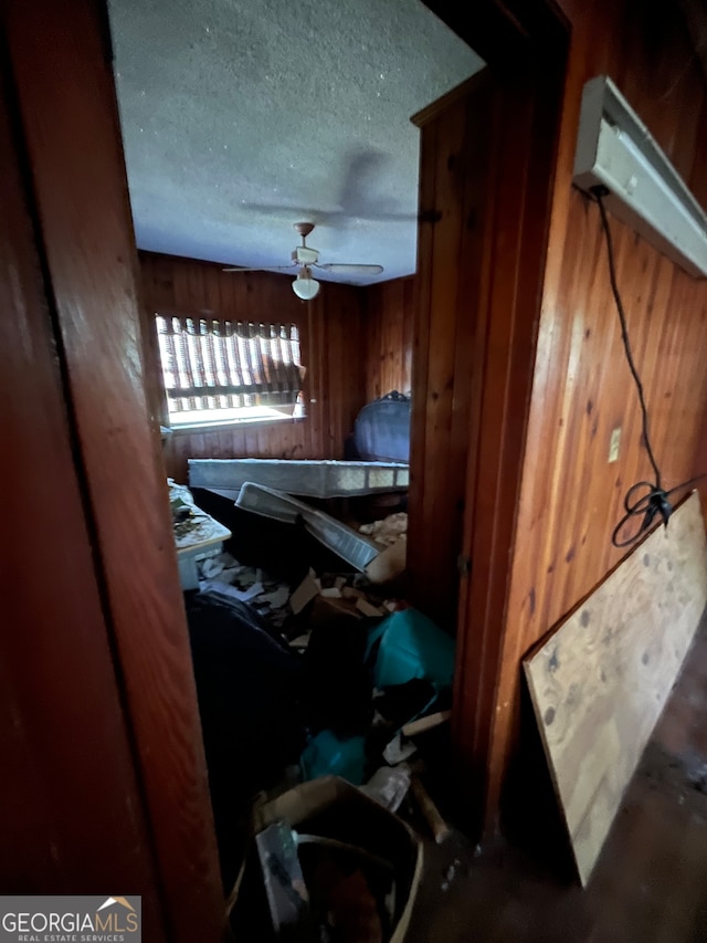 interior space with ceiling fan, a textured ceiling, and wooden walls