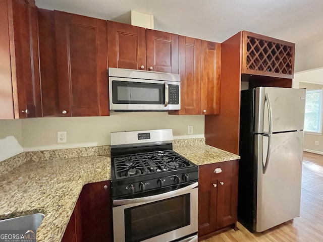 kitchen with light stone countertops, appliances with stainless steel finishes, and light hardwood / wood-style floors