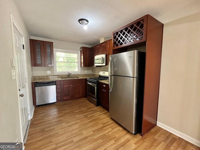 kitchen featuring stainless steel appliances, sink, light hardwood / wood-style flooring, and light stone counters