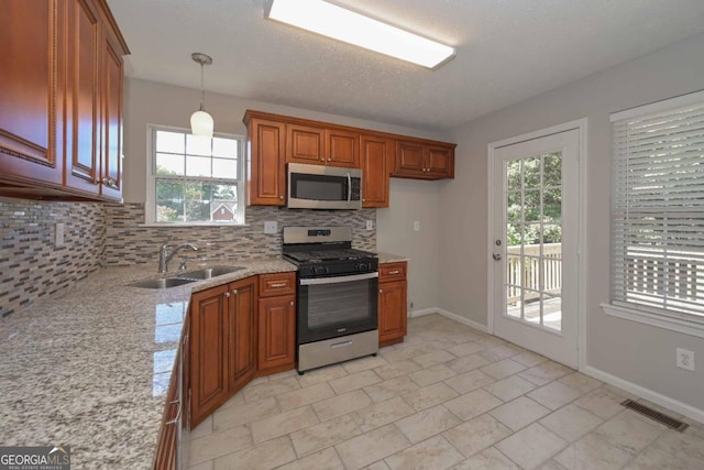 kitchen with appliances with stainless steel finishes, a wealth of natural light, backsplash, and pendant lighting