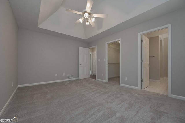 unfurnished bedroom featuring a walk in closet, a closet, light carpet, ceiling fan, and connected bathroom