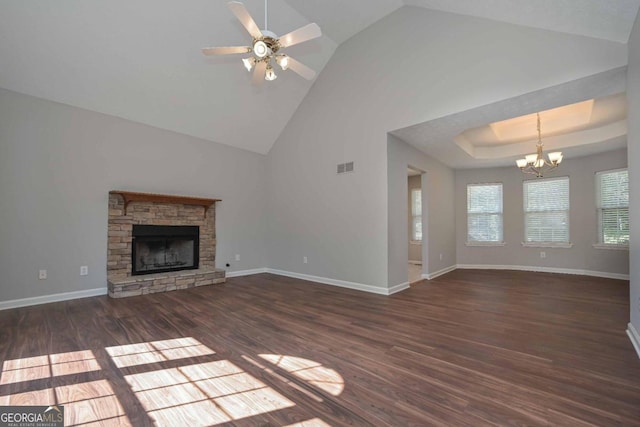 unfurnished living room featuring ceiling fan with notable chandelier, a stone fireplace, a tray ceiling, dark hardwood / wood-style flooring, and high vaulted ceiling