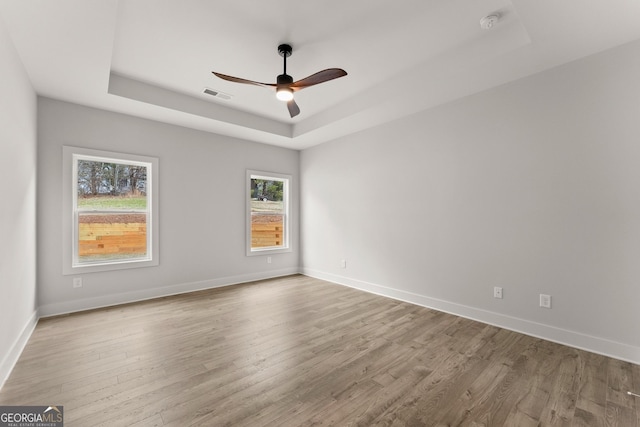 empty room with ceiling fan, light hardwood / wood-style floors, and a raised ceiling