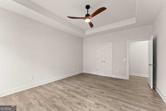 unfurnished bedroom featuring ceiling fan, light hardwood / wood-style floors, and a raised ceiling