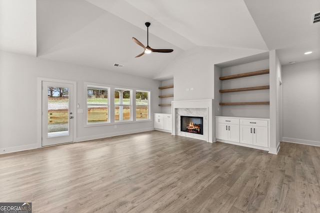 unfurnished living room featuring a premium fireplace, ceiling fan, lofted ceiling, and light wood-type flooring