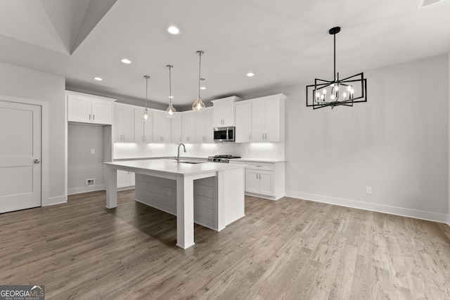 kitchen with white cabinets, decorative light fixtures, a center island with sink, and sink