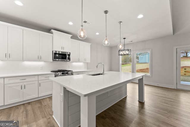 kitchen with white cabinets, appliances with stainless steel finishes, an island with sink, and sink