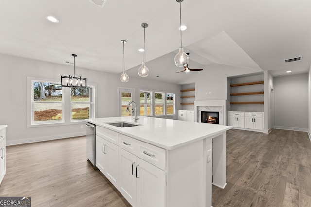 kitchen with a high end fireplace, sink, light hardwood / wood-style flooring, white cabinetry, and an island with sink