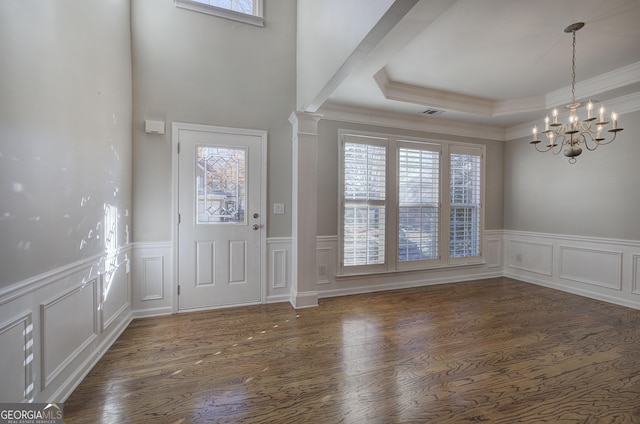 foyer featuring a notable chandelier, a raised ceiling, ornate columns, and dark wood-type flooring