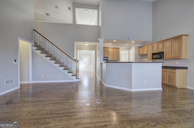 kitchen featuring light brown cabinetry, dark wood-type flooring, and a high ceiling