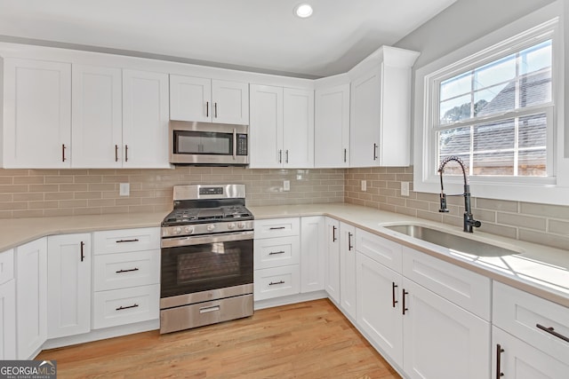 kitchen with sink, white cabinetry, stainless steel appliances, and light hardwood / wood-style floors