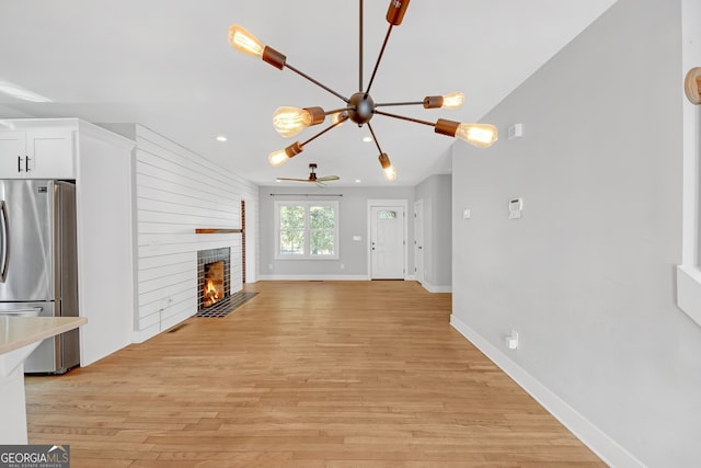 unfurnished living room featuring light hardwood / wood-style flooring, a fireplace, and ceiling fan with notable chandelier