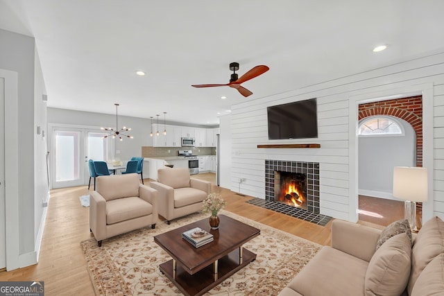 living room with ceiling fan with notable chandelier, a fireplace, and light hardwood / wood-style floors