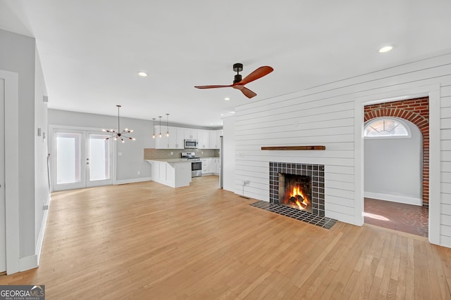 unfurnished living room with a tiled fireplace, light wood-type flooring, and ceiling fan with notable chandelier