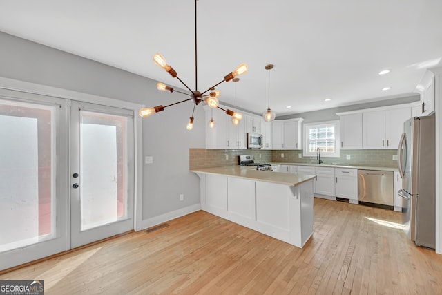 kitchen featuring kitchen peninsula, hanging light fixtures, white cabinetry, light hardwood / wood-style flooring, and stainless steel appliances