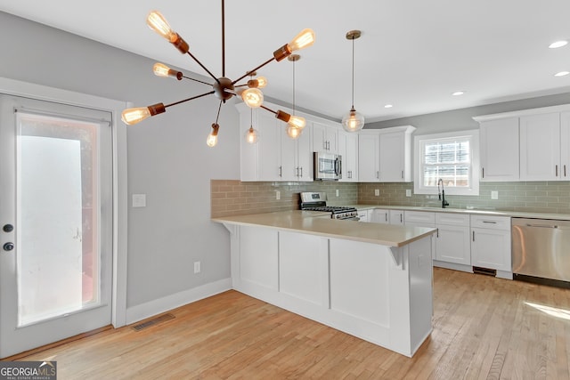 kitchen featuring light hardwood / wood-style flooring, kitchen peninsula, sink, white cabinetry, and appliances with stainless steel finishes