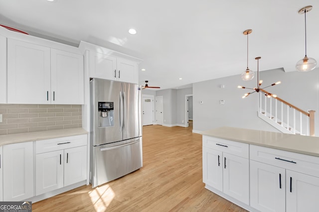 kitchen featuring light hardwood / wood-style flooring, backsplash, stainless steel fridge, decorative light fixtures, and white cabinets