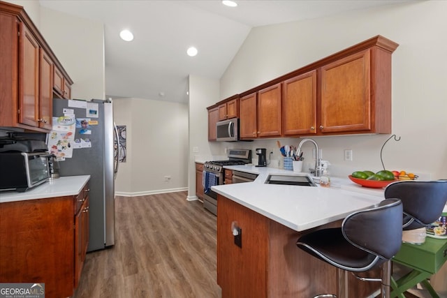 kitchen with a kitchen breakfast bar, stainless steel appliances, sink, vaulted ceiling, and light hardwood / wood-style floors