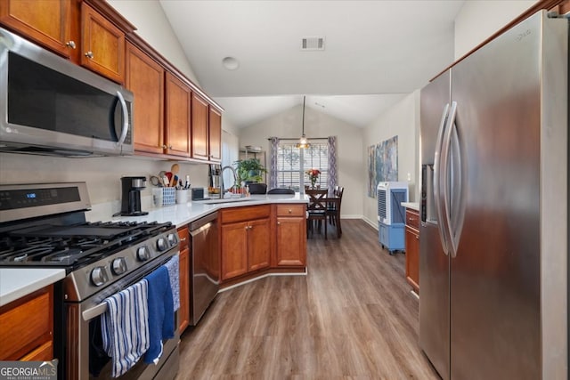 kitchen featuring sink, stainless steel appliances, lofted ceiling, pendant lighting, and light hardwood / wood-style flooring