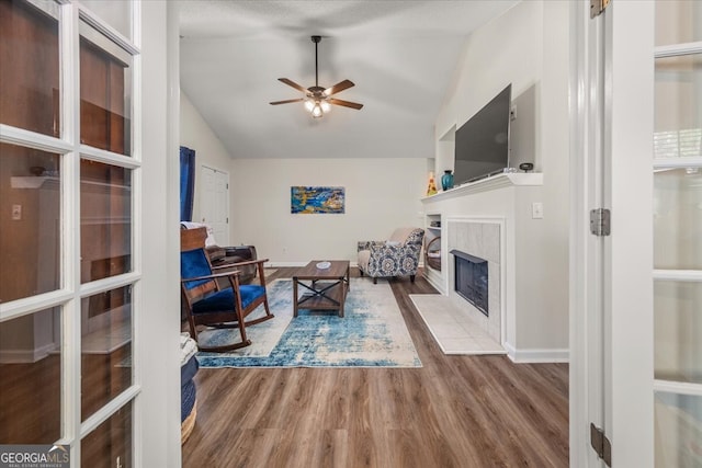 living room featuring lofted ceiling, hardwood / wood-style flooring, a tile fireplace, and ceiling fan