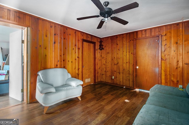 sitting room with wood walls, dark hardwood / wood-style floors, and ceiling fan