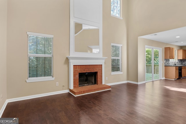 unfurnished living room featuring a towering ceiling, hardwood / wood-style flooring, sink, and a fireplace