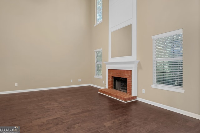 unfurnished living room featuring a high ceiling, a brick fireplace, and dark hardwood / wood-style floors