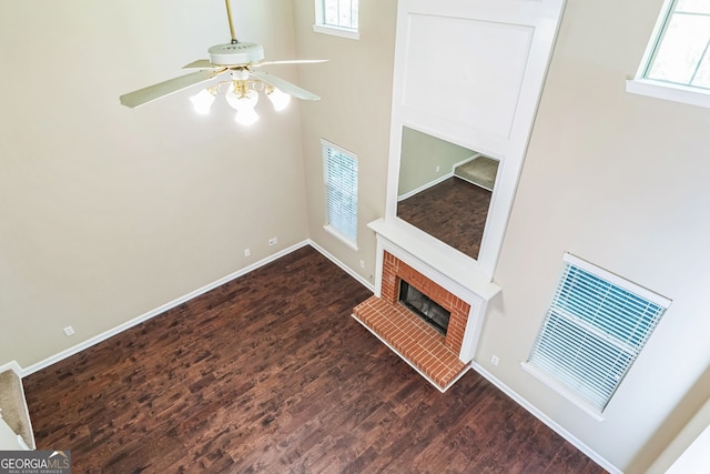 unfurnished living room featuring ceiling fan, dark wood-type flooring, and a brick fireplace