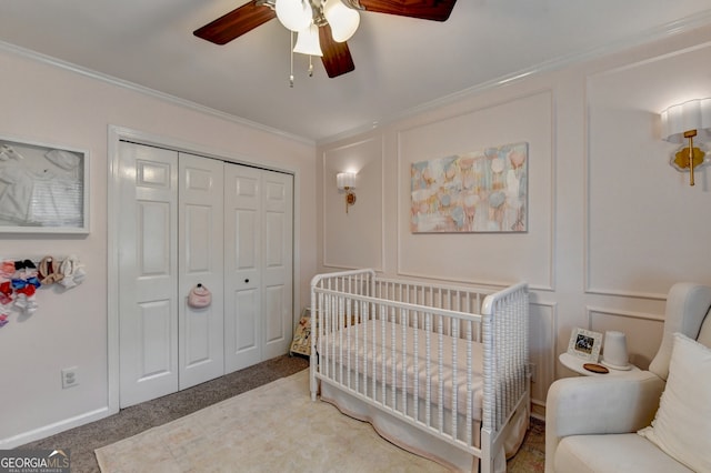 bedroom featuring carpet, ceiling fan, a closet, a crib, and crown molding