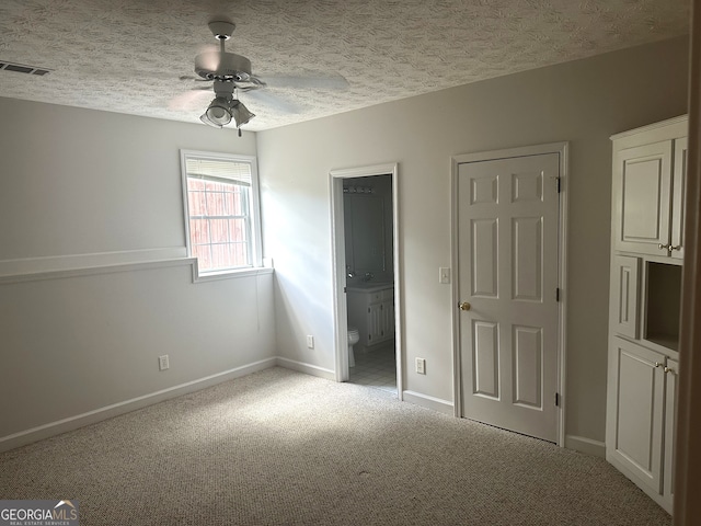 unfurnished bedroom with connected bathroom, ceiling fan, a textured ceiling, and light colored carpet