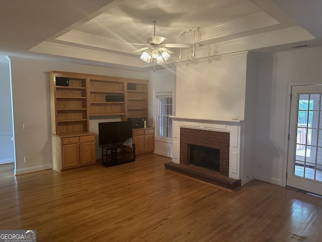 unfurnished living room with dark hardwood / wood-style floors, a tray ceiling, ornamental molding, a fireplace, and ceiling fan