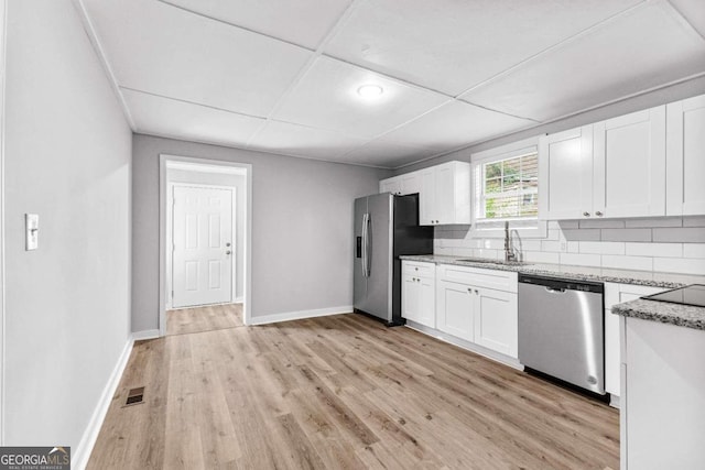 kitchen with appliances with stainless steel finishes, sink, light stone countertops, white cabinetry, and light hardwood / wood-style flooring