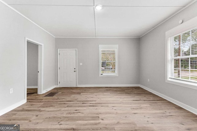 empty room with crown molding, light wood-type flooring, and a wealth of natural light