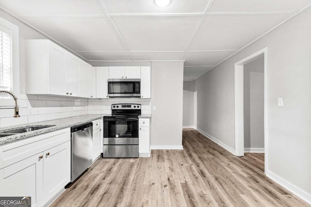 kitchen with appliances with stainless steel finishes, white cabinetry, light stone countertops, light hardwood / wood-style floors, and sink