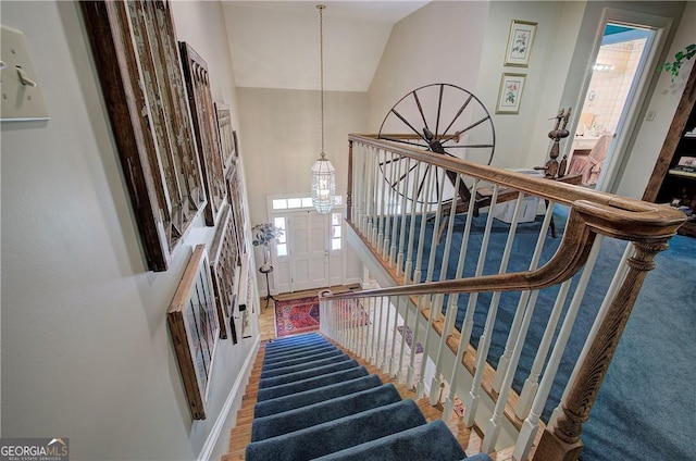 staircase featuring a notable chandelier, wood-type flooring, and lofted ceiling